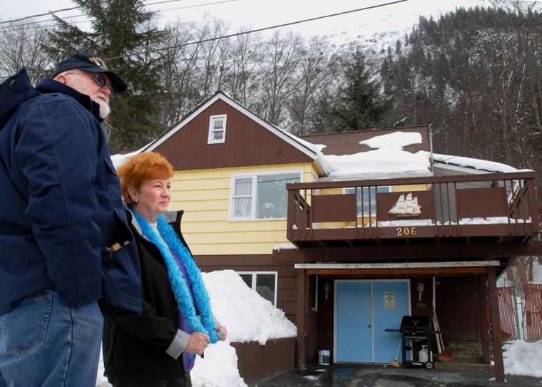 Carroll \"Butch\" Holst  and his wife Janice  stand in front of their home, March 20, 2007 in Juneau, Alaska. The Holsts were thrilled in 1978 when they bucked a tight housing market and sealed a deal on a nice affordable home in downtown Juneau. Thrilled, that is, until someone showed them a picture of their new house on the cover of National Geographic in a story that tagged their neighborhood as North America's worst avalanche risk.(AP Photo/Chris Miller)