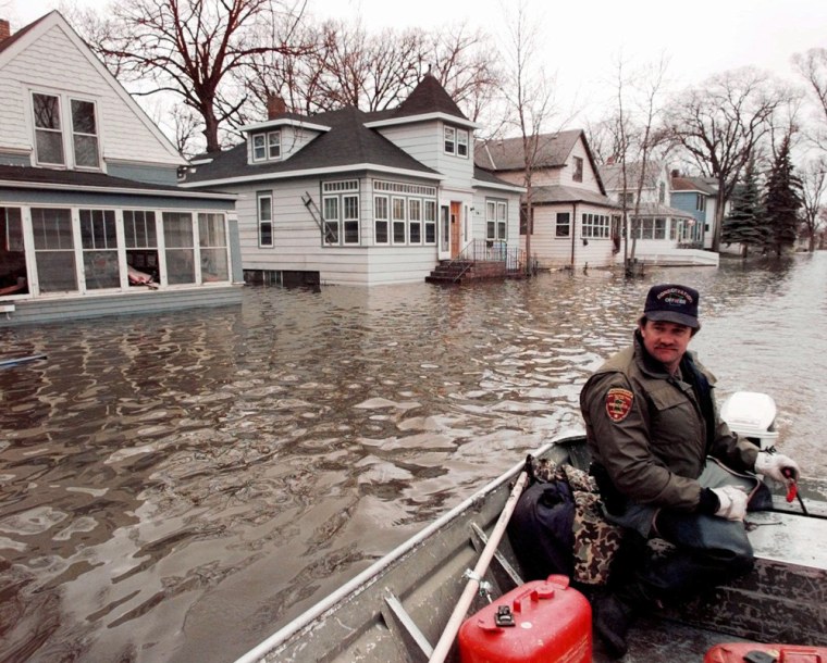 ** FILE ** Conservation Officer Keith Backer patrols an area of East Grand Forks, Minn., via boat April 29, 1997. Many East Grand Forks homes and businesses remained under floodwaters left by the Red River. The flooding river forced thousands to flee their homes iin Minnesota and neighboring Grand Forks, N. D. Ten years later, heavy rain and snow still make people nervous but a dike system has helped ease some fears. (AP Photo/Eric Gay)