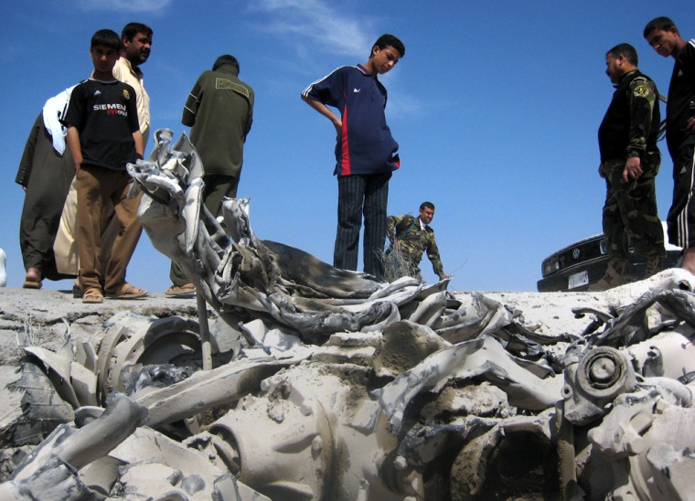 Iraqis stand Wednesday beside wreckage of a fuel tanker that exploded the day before at a police checkpoint outside Ramadi, west of Baghdad, Iraq. 