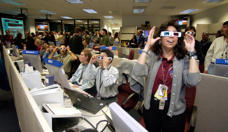 Men and women of the Mars Exploration Rover mission admire some of the Spirit rover's images in 3-D.  Nagin Cox, then deputy team chief of the spacecraft rover engineering team, dons 3-D glasses with wrists adorned with four watches: one that tells the time on Earth, one for Spirit's time zone, one for Opportunity's time zone and one special "actiwatch" that was part of a fatigue study run by NASA.