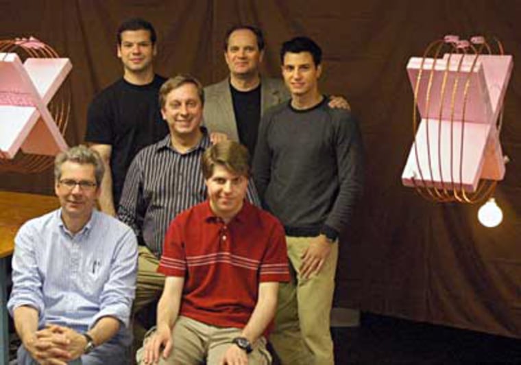 Wireless power is transmitted over a 7-foot distance from the coil on the left to the coil on the right, where it powers a 60-watt light bulb. The researchers are obstructing the direct line of sight between the coils. Front row: Peter Fisher and Robert Moffatt; second row: Marin Soljacic; third row: Andre Kurs, John Joannopoulos and Aristeidis Karalis. 