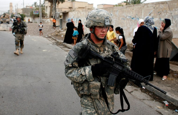 U.S. soldiers walk past Iraqi women with their children during a patrol in Baghdad