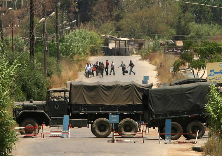 Two Lebanese army trucks block the road of the southern entrance of the Palestinian refugee camp Wednesday, as Palestinian carrying their belongings flee from the camp of Nahr el-Bared, in the northern city of Tripoli, Lebanon.