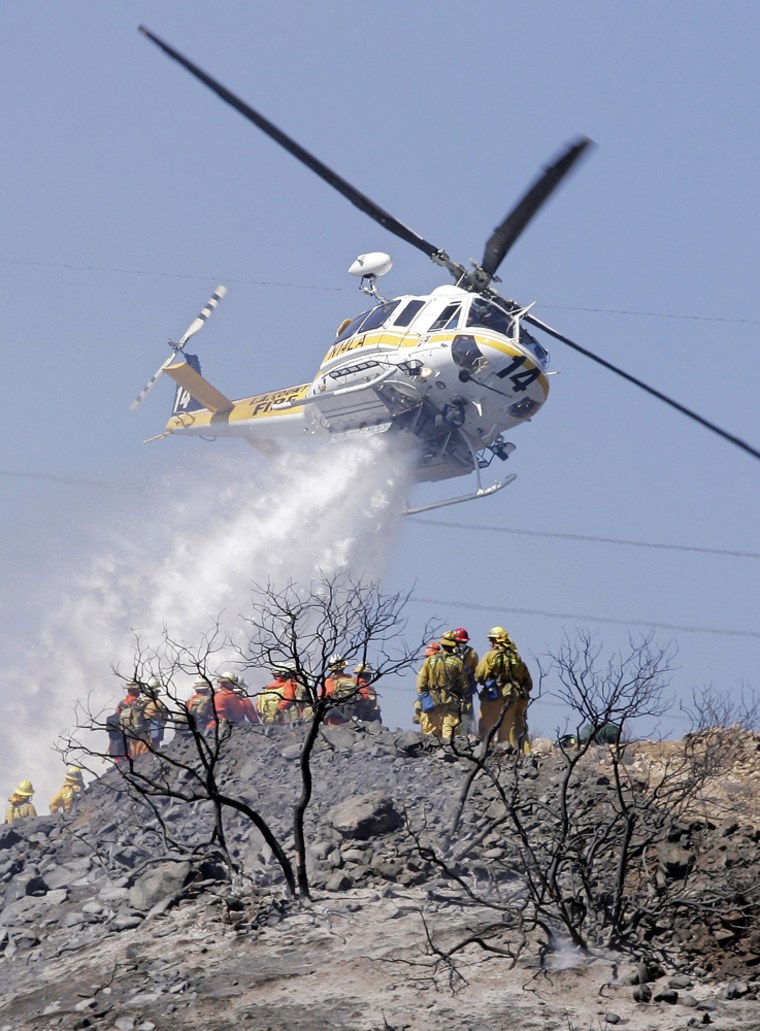 A Los Angeles County fire helicopter drops water on a brush fire Wednesday as firefighters look on in the Sun Valley area of Los Angeles.