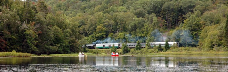 Canoeists watch the Adirondack Scenic Railroad train as they paddle on Moose River outside Old Forge, N.Y. 