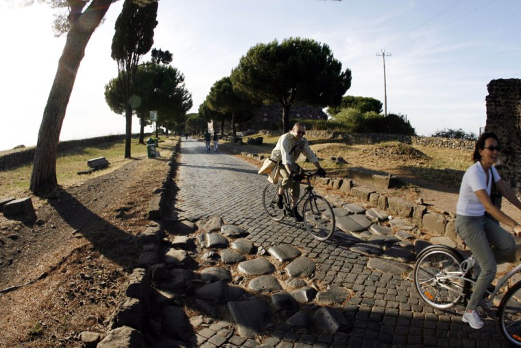 Bicyclists ride along the Appian Way in Rome. The Appian Way was begun as a military highway in 312 B.C. by the statesman Appius Claudius. Paved with huge lava blocks in a bed of crushed stone cemented with lime, the roadway was wide enough to allow two chariots to pass. Soon it stretched some 350 miles to the Adriatic port of Brundisum (now Brindisi) at the heel of Italy's boot.