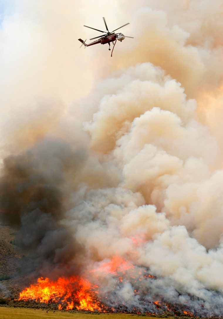 A helicopter with a water tank makes a drop on the Salt Creek Fire on Sunday near Nephi, Utah. The Sanpete County Sheriff's Office advised residents of Fountain Green, southeast of Nephi, to evacuate Sunday night when the wind shifted to the south, but lifted the notice when the wind shifted again.