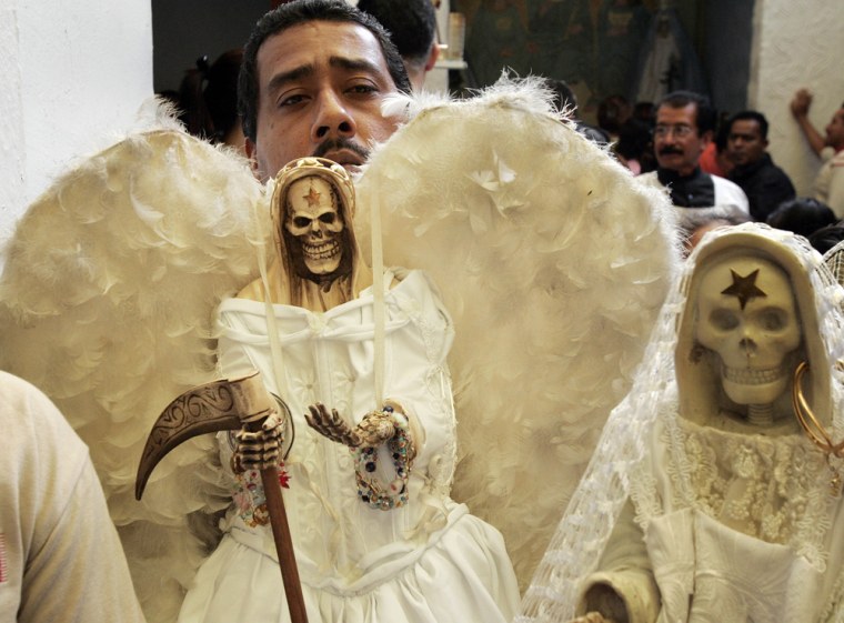 A man holds a skeletal figure representing the folk saint known in Mexico as "Santa Muerte," or "Saint of Death." 
