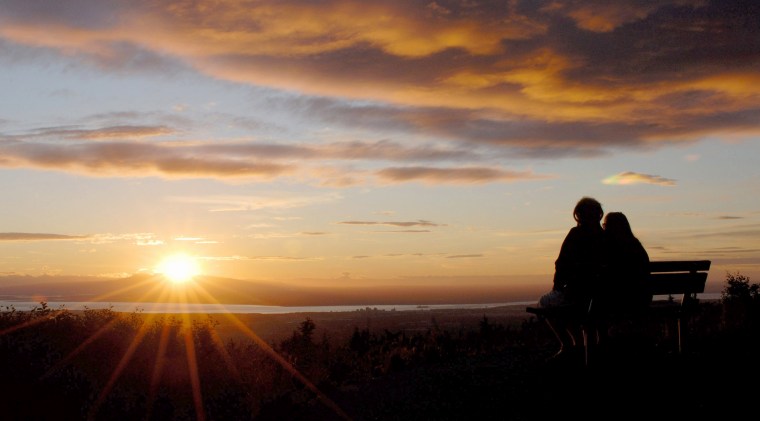 A couple watches the sun setting over Mount Susitna in the foothills of the Alaska Range from the vantage point of the Glen Alps overlook in Chugach State Park in Anchorage, Alaska. 