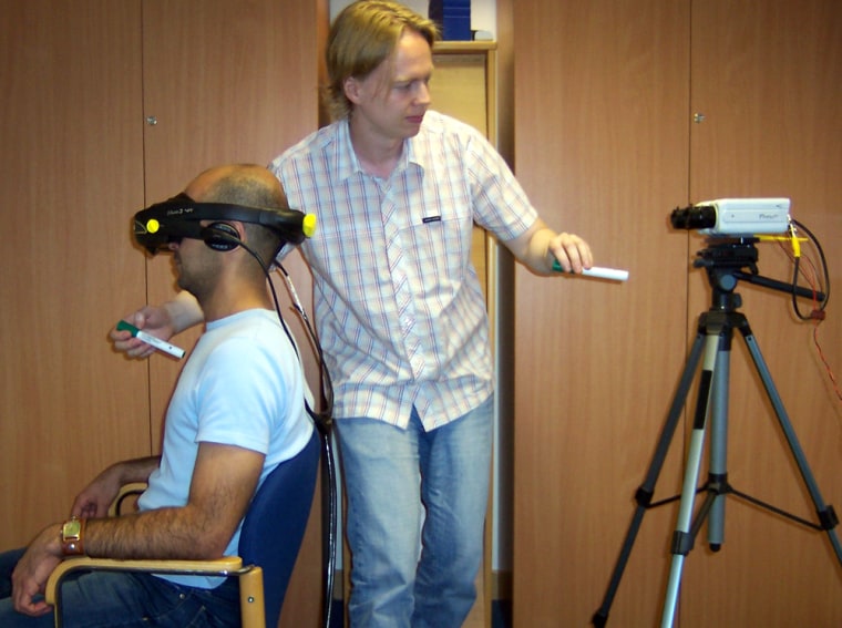A volunteer wearing virtual-reality goggles watches the back of his own body, as seen from behind by the camera. He is also watching a plastic rod moving toward a location just below the camera, while his real chest is simultaneously touched in the corresponding spot. The subject typically felt as if he was being poked in the chest while he was outside his body.