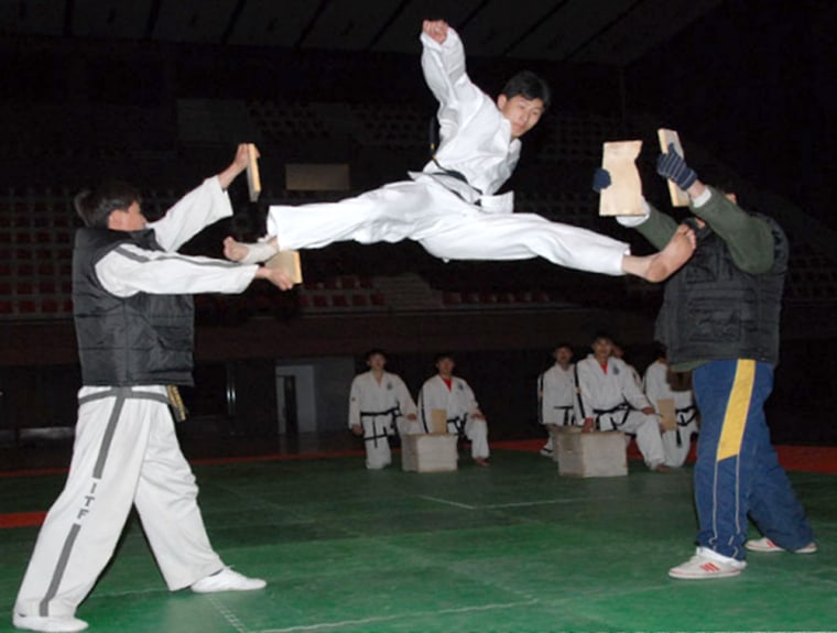 A member of the North Korean tae kwon do team breaks two boards while executing a flying kick.