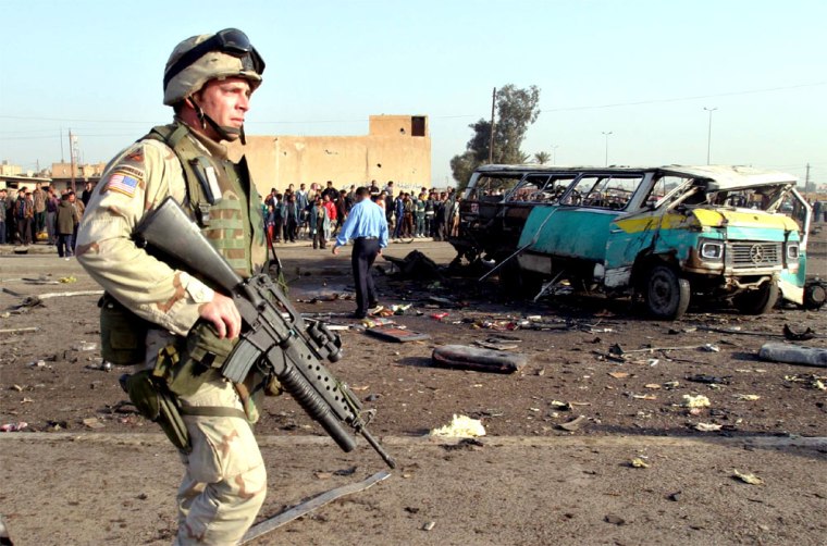 A U.S. SOLDIER GUARDS WRECKAGE OF A MINIBUS AFTER AN EXPLOSION IN BAGHDAD