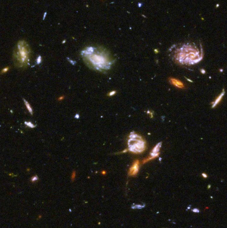 Three galaxies just below center are enmeshed in battle, their shapes distorted by the brutal encounter