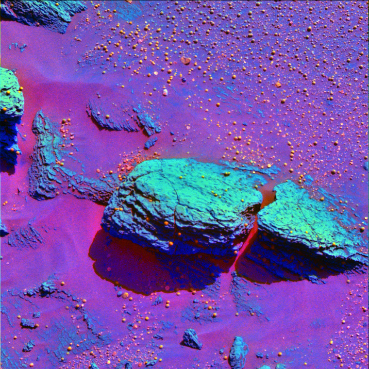 A false-color image from the Opportunity rover, released Feb. 9, accentuates the differences between a green-looking slab of Martian bedrock and orange-looking spheres of rock.  Scientists compared the \"spherules\" to blueberries embedded within and scattered around muffins of bedrock.  The spherules could have been created by volcanic eruptions, cosmic impacts or the percolation of mineral-laden water through the bedrock layers.