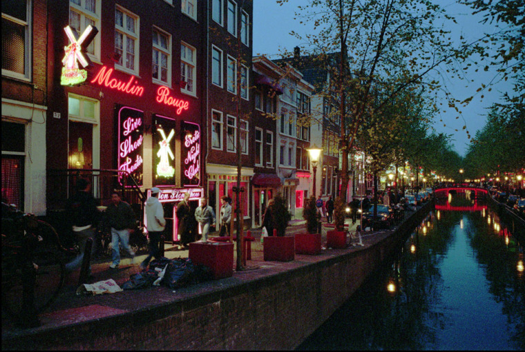 FILE - Prostitutes stand behind red-lit windows, waiting for customers in Amsterdam's Red Light district in this May 2, 1996 file photo. With its scantily-clad prostitutes posing in brothel windows and coffee shops oozing the pungent aroma of cannabis smoke, Amsterdam's Red Light District has always thrived on its illicit atmosphere. But while the city has long tolerated coffee shops where marijuana is sold openly and fully legalized prostitution, authorities say the network of cobbled alleys and canals is a haven for organized crime where mobsters launder money through real estate, brothels and bars. \"We are very worried about the mixing of the underworld with the above board in the center of Amsterdam,\" the city said Thursday in a press release. \"Particularly in the Red Light District, money laundering from real estate... and involvement of organized crime in prostitution, coffee shops, smart shops, and parts of the hotel industry is a cause for concern.\" The problem is well-known, but f