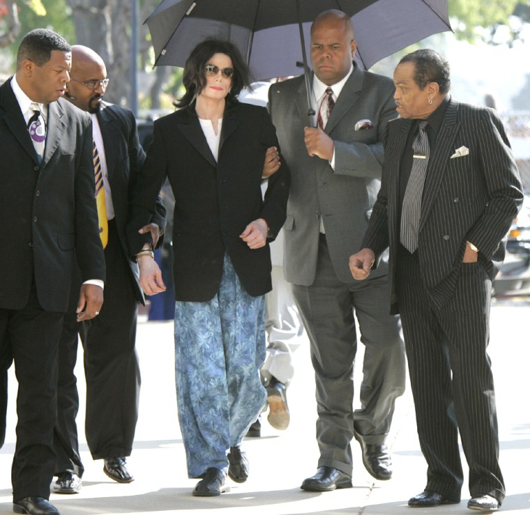 Michael Jackson wears pajama pants and is aided by bodyguards upon arrival