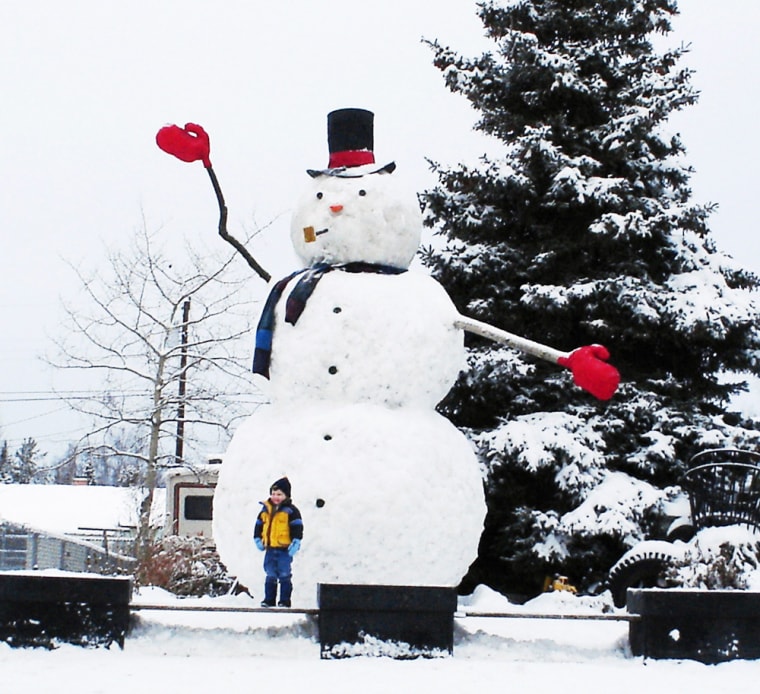 Young boy poses in front of snowman in residential neighborhood in Anchorage