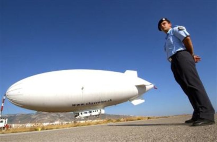 A Greek police officer stands in front of a blimp at an old airfield in Athens. The airship, fitted with cameras and sensors, will help provide security at the Athens Olympics. 