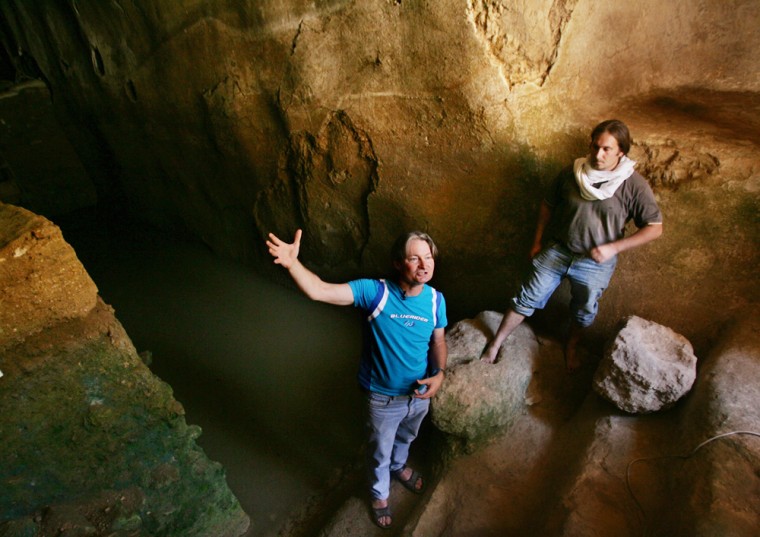 British archaeologist Shimon Gibson, left, gestures with a wave of his hand, and site manager Rafi Lewis places his foot in a ceremonial stone as they stand in a large cistern, in the cave where the excavation team believes John the Baptist anointed many of his disciples.