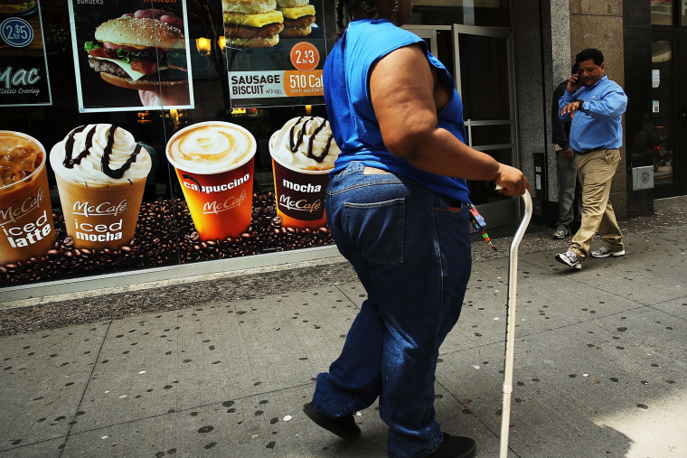Image: A woman walks by a sign advertising sugary drinks