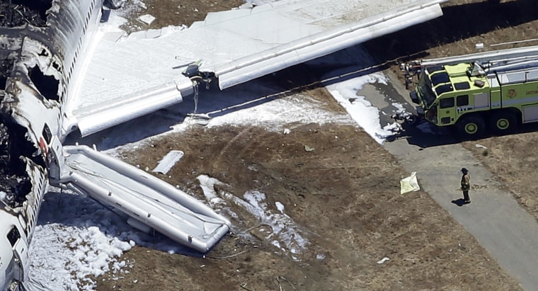 Image: A firefighter stands by a tarpaulin sheet covering a body near the wreckage of the Asiana Flight 214