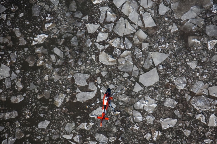 Image: A Coast Guard helicopter flies along the Hudson River, which is full of ice floes