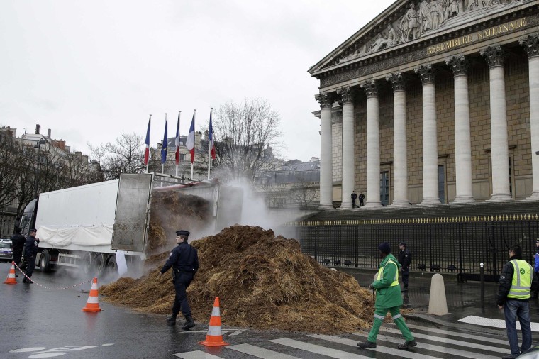 Image: French police and municipal workers walk near a large pile of manure sits in front of the National Assembly in Paris.