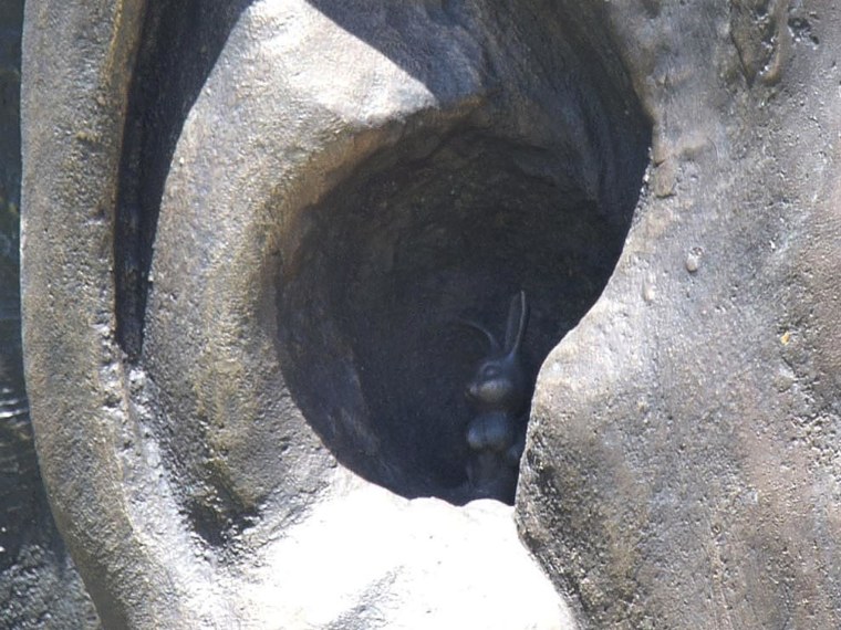 Image: A sculpted rabbit tucked inside one of the bronze ears of a statue of Nelson Mandela.