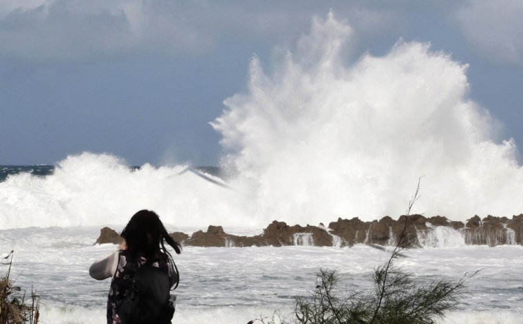 Image: A woman watches large waves crash onto the shore at Shark's Cove as high surf hits the north shore of Hawaii.