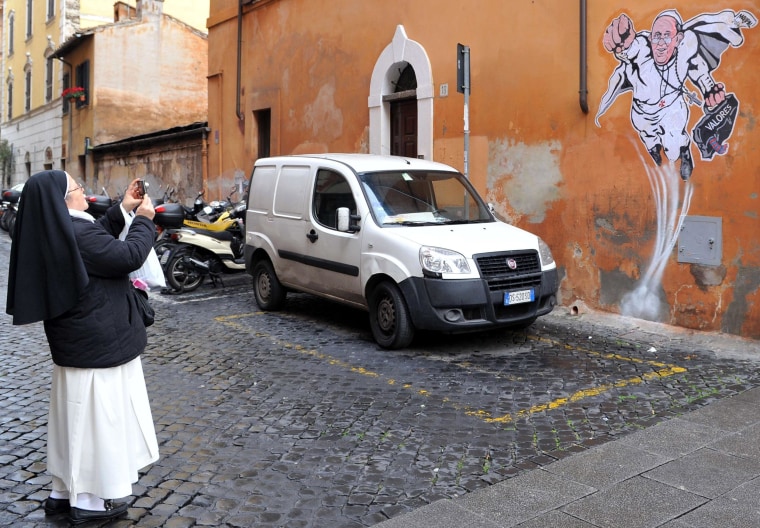 Image: A nun takes a picture of a street art mural of Pope Francis as a superman.
