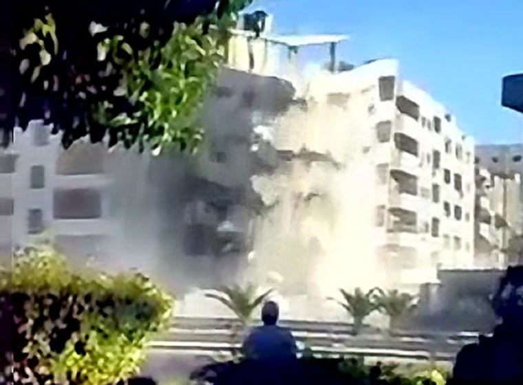 A video screenshot shows government soldiers and civilian contractors overseeing the demolition of a seven story residential apartment building with controlled explosions in the Zahirat neighborhood of Damascus. Video recorded late September 2012.