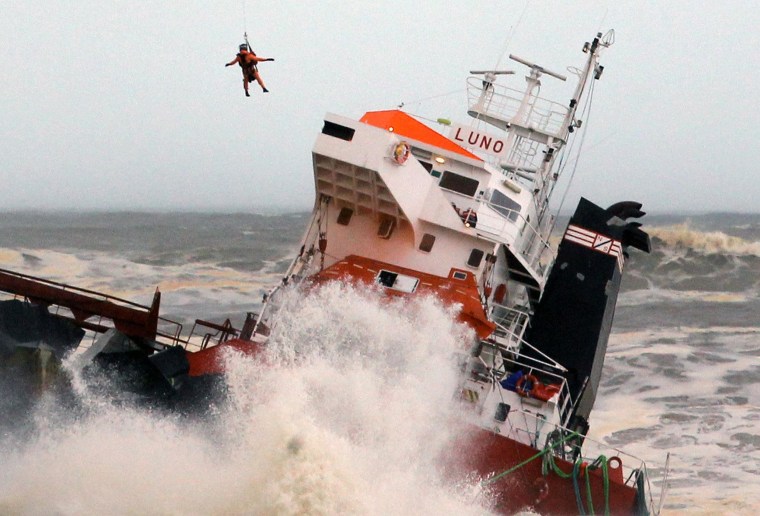 Image: A helicopter lowers a rescue worker toward Spanish cargo ship The Luno which slammed into a jetty