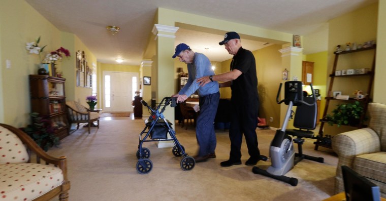 Image: Caregiver Warren Manchess, right, walks across the living room with Paul Gregoline, 92, in Noblesville, Ind. on Nov. 27, 2013.