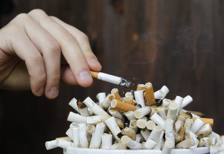 Image: A man taps ashes off his cigarette into an ashtray.