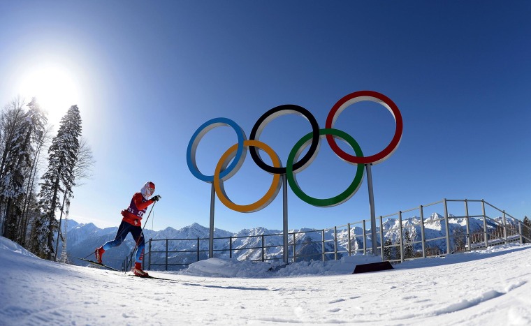Image: A cross-country skier practices underneath the Olympic rings.