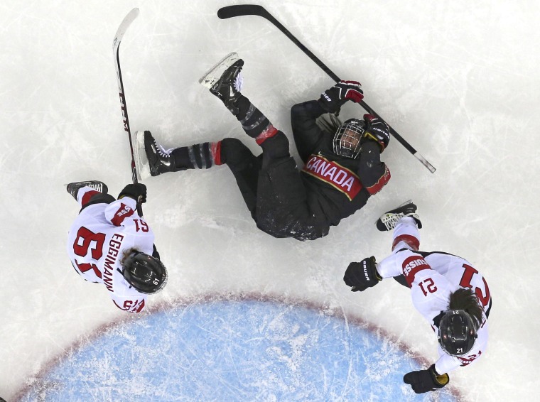 Canada's Spooner is knocked to the ice by Switzerland's Eggimann and Benz during the second period of their women's ice hockey game at the 2014 Sochi Winter Olympics