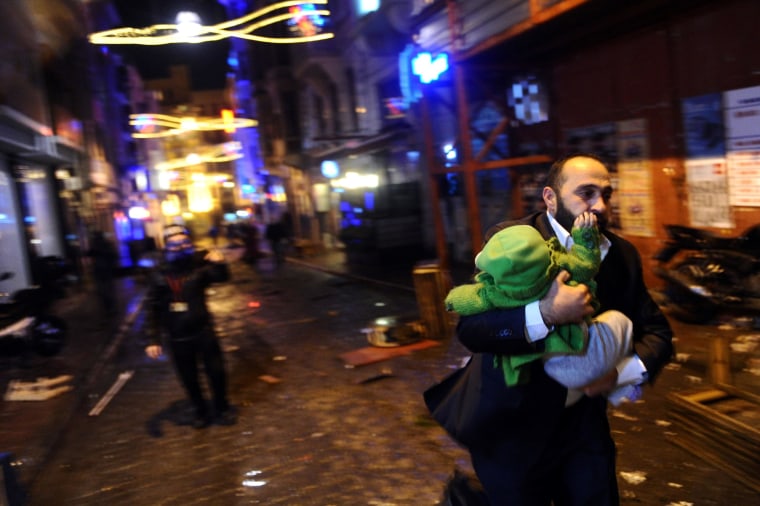 Image: A man carrying a baby runs away from tear gas