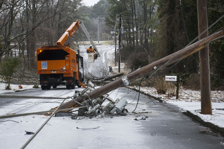 Image: Workers remove trees and snapped power poles brought down in the road in Doraville, Ga.