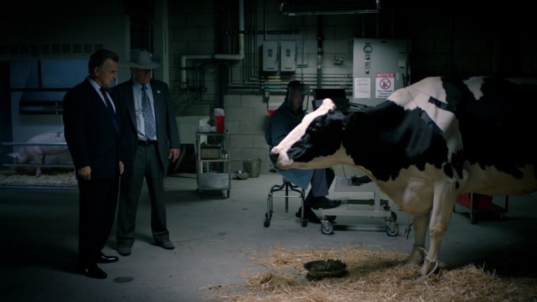 Buck Marshall (Ray Wise) and Mick Mitcherson (Eric Pierpoint) discuss the introduction of PetroPellet in "Farmed and Dangerous" while a cow overhears.