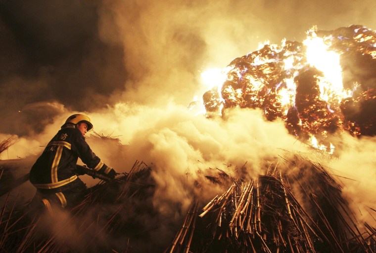 Image: A firefighter attempts to extinguish a fire which broke out on piles of reed at a paper factory in Changde
