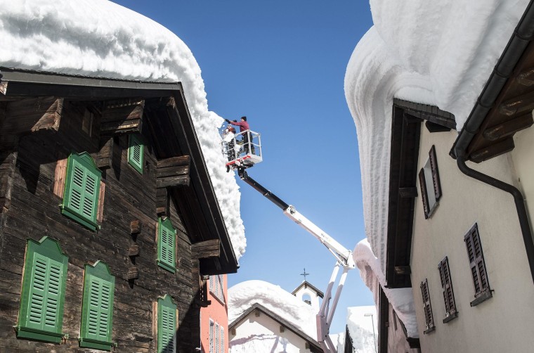 Image: Municipal workers clear snow off buildings in the village of Bedretto in Ticino, Switzerland.