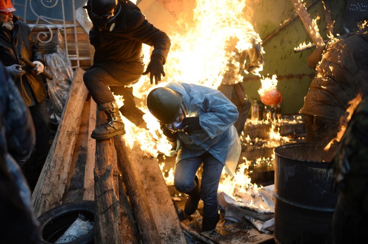 Image: Protesters try to protect themselves from fire as they stand behind burning barricades during clashes with police