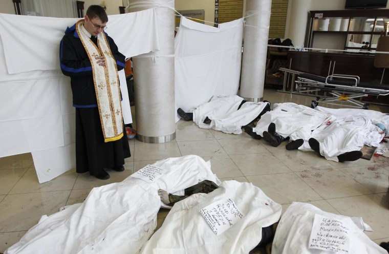 Image: A priest stands in the lobby of the hotel Ukraine near bodies of anti-government protesters killed during clashes with riot police in Kiev