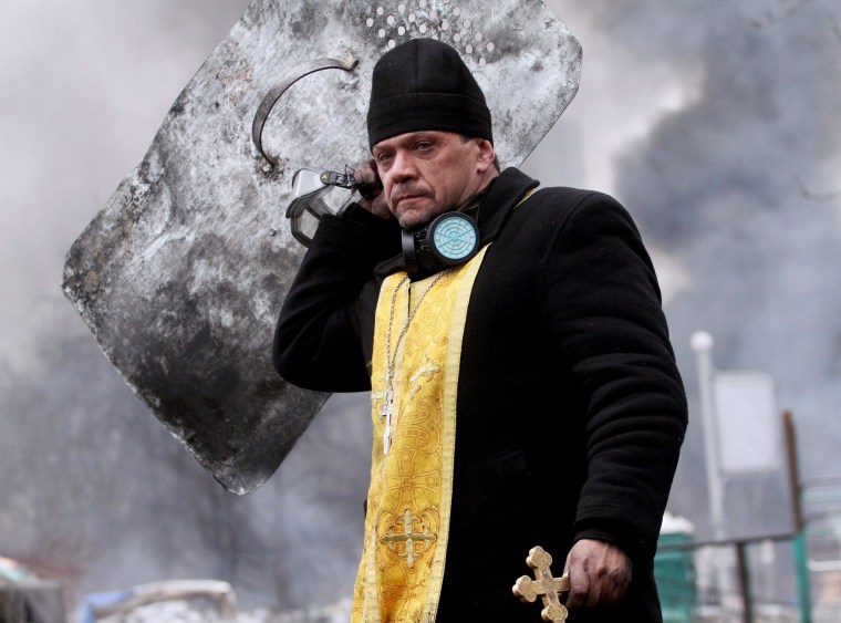 Image: A priest holds a cross and shield during clashes betwwen anti-government protesters and riot police in central Kiev