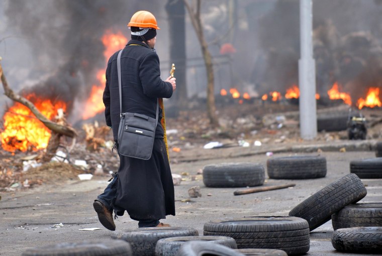 Image: An Orthodox priest walks under fire during clashes between anti-government protesters and riot police in central Kiev