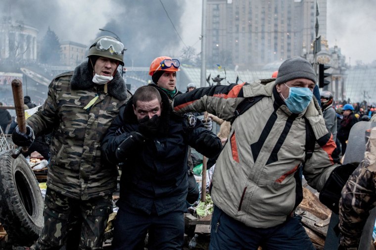 Image: Anti-government demonstrators escort a captured police officer in Kiev