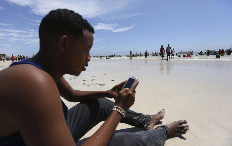 Image: A Somali man browses the internet on his mobile phone at a beach along the Indian Ocean coastline in Mogadishu