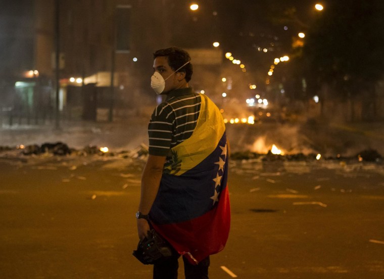 A man is wrapped in the Venezuelan flag as he stands close to a fire at a barricade during a protest against Venezuelan government in Altamira, Caracas, Venezuela, 20 February 2014.