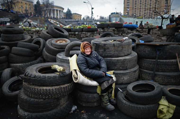 Image: An elderly woman sits on tires at a barricade in Independence Square