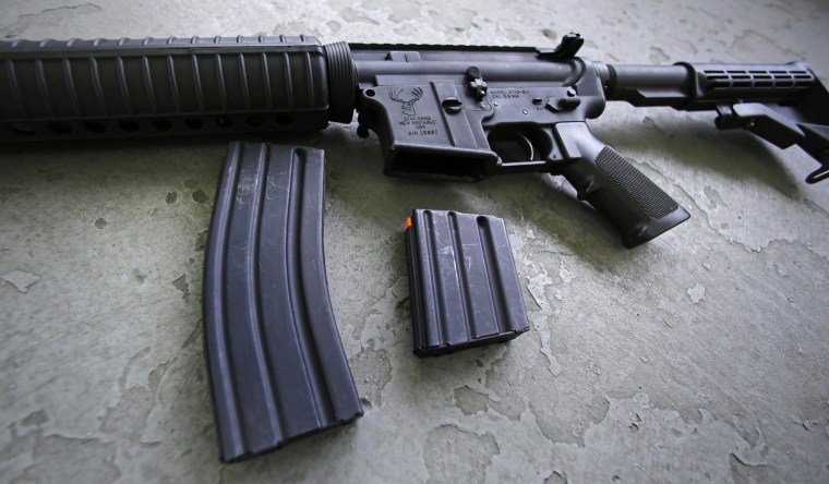 A 30 round magazine, left, and a 10 round magazine, right, rest below an AR-15 rifle.